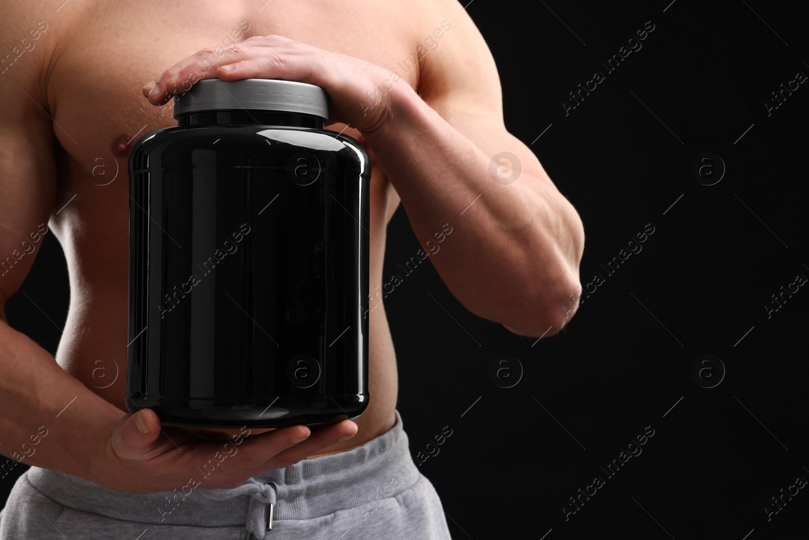 Photo of Young man with muscular body holding jar of protein powder on black background, closeup. Space for text