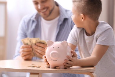 Photo of Family with piggy bank and money at table indoors