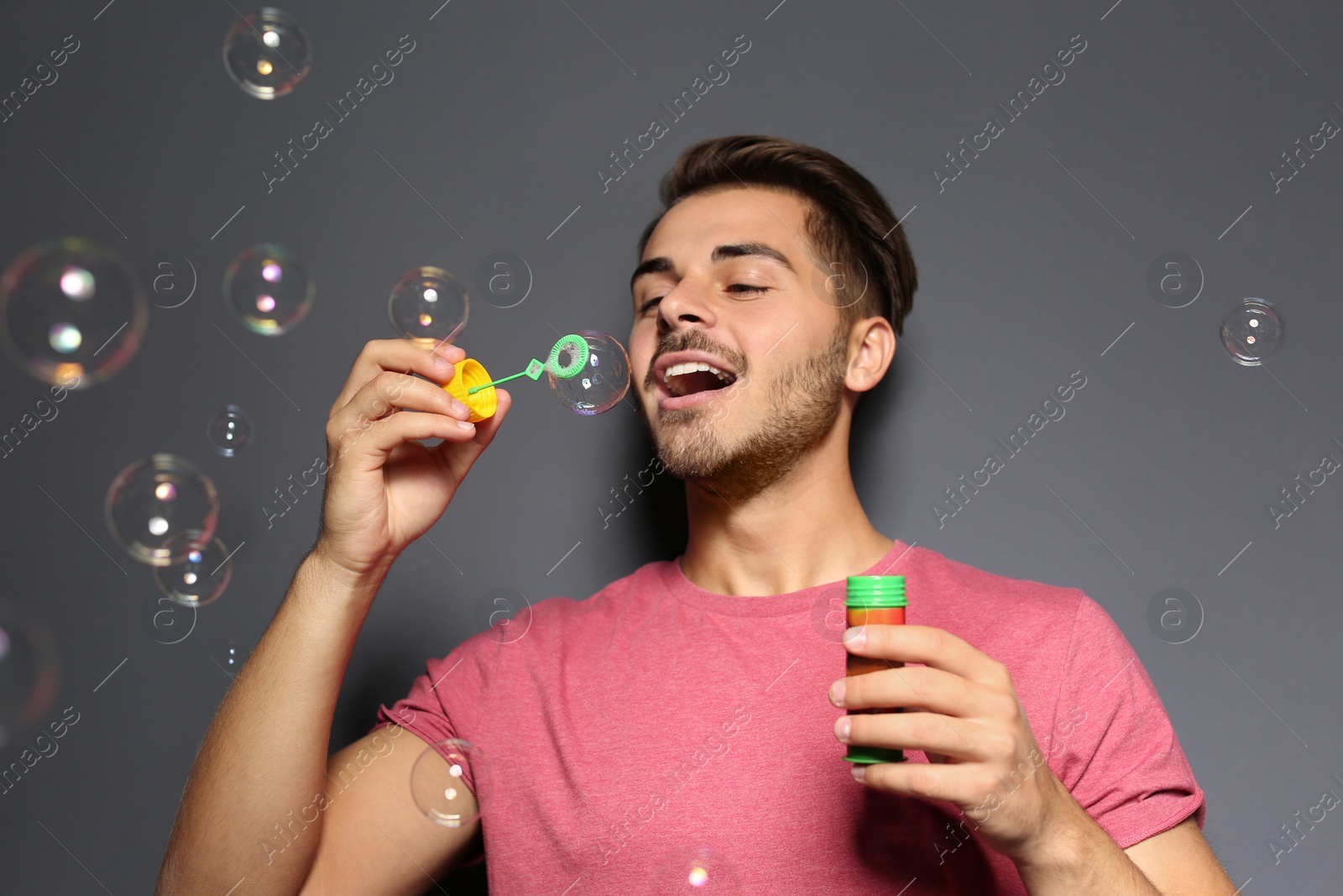 Photo of Young man blowing soap bubbles on color background