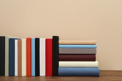 Many different hardcover books on wooden table near beige wall