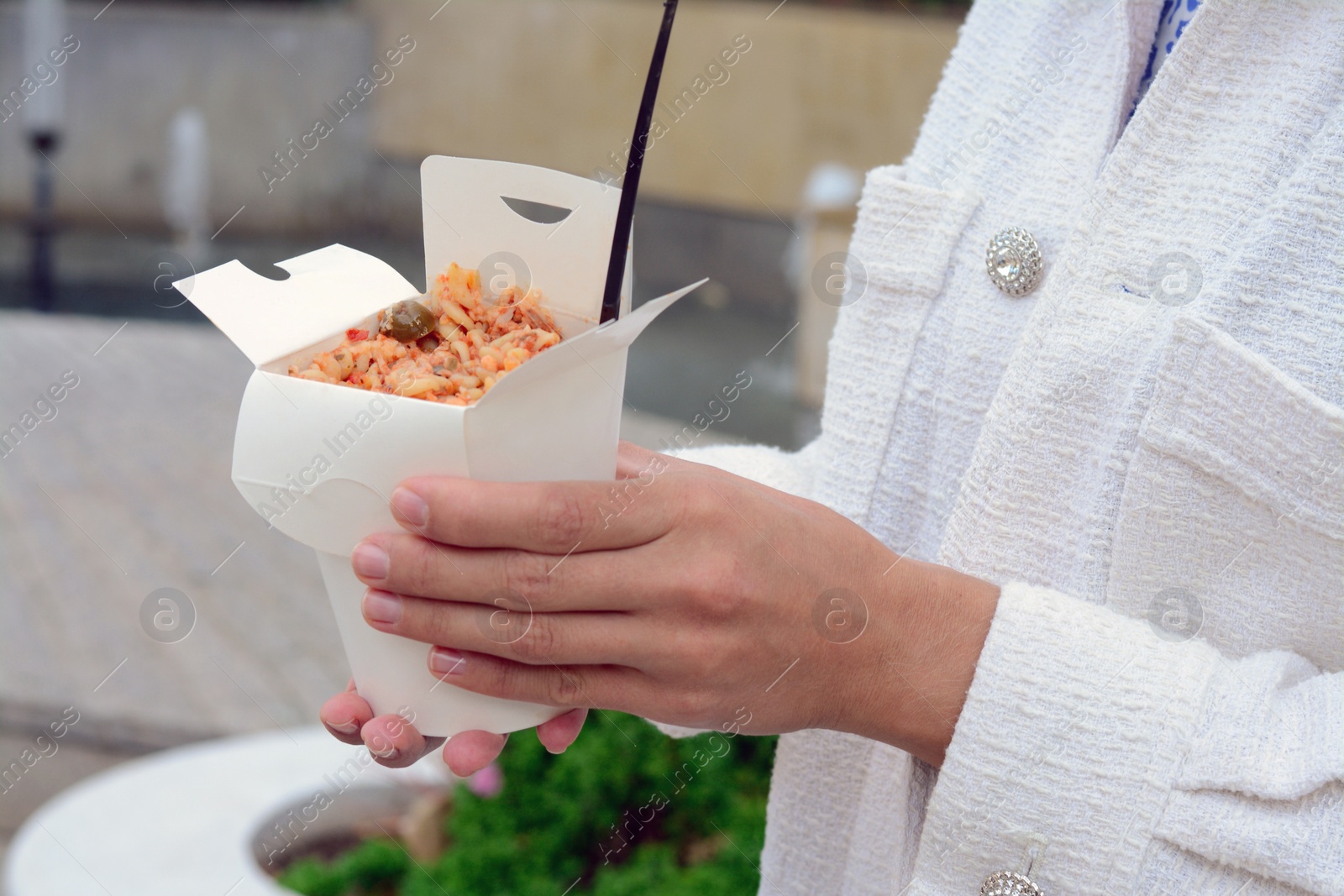 Photo of Woman holding paper box of takeaway noodles with fork outdoors, closeup. Street food