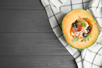 Photo of Half of melon with prosciutto, blueberries and herbs on grey wooden table, flat lay