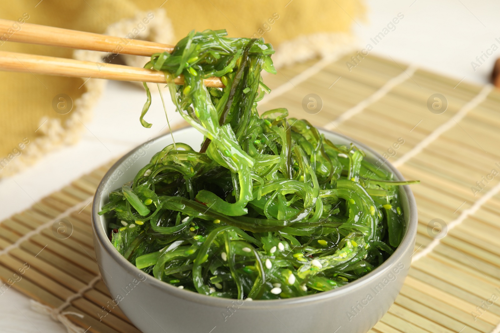 Photo of Chopsticks with Japanese seaweed salad in bowl on table, closeup