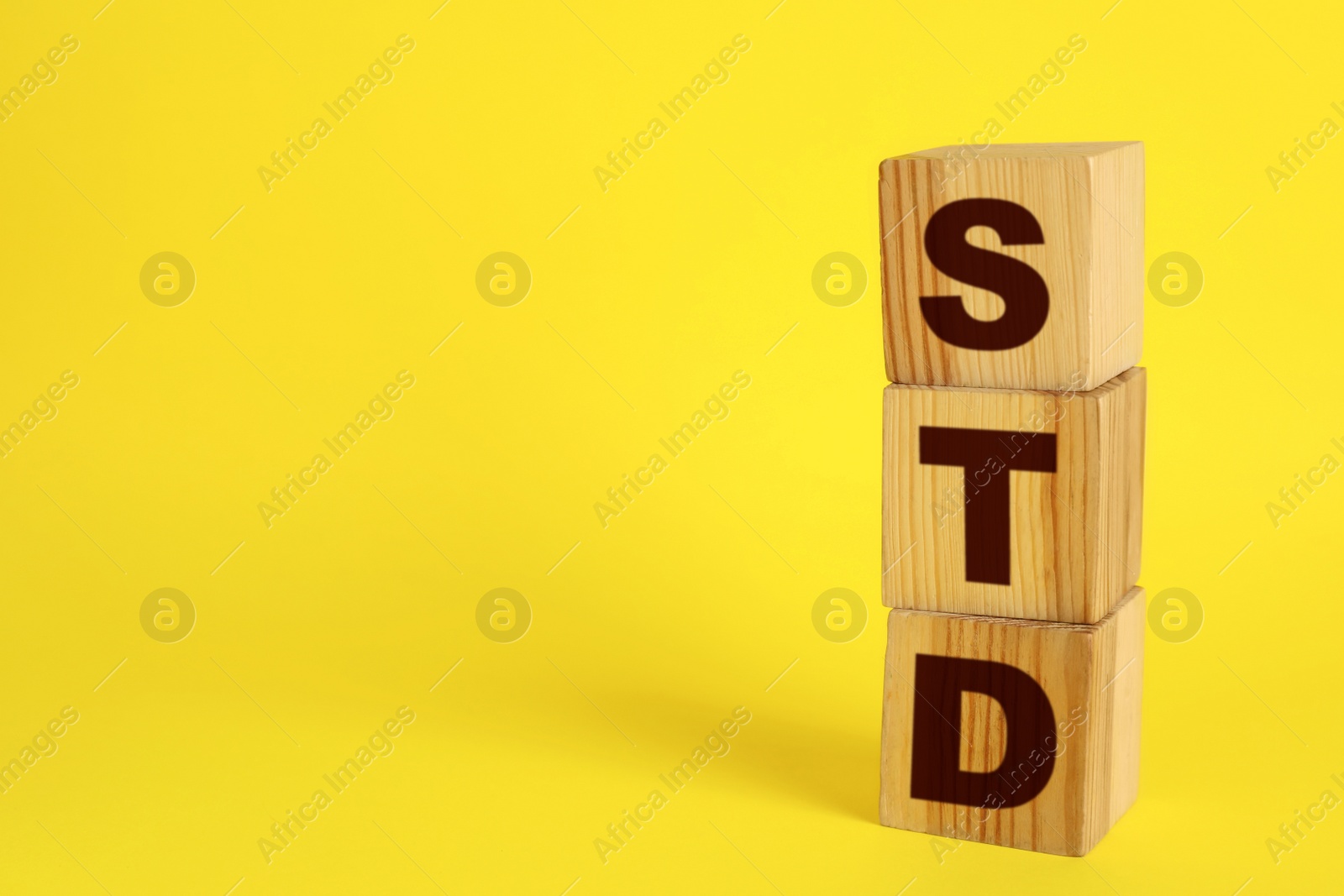 Photo of Abbreviation STD made with wooden cubes on yellow background, space for text