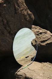 Round mirror reflecting sea on stones outdoors