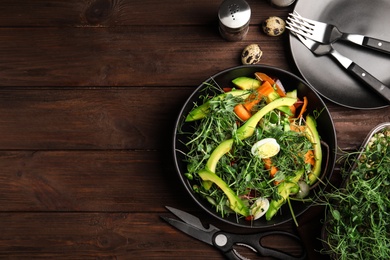 Salad with fresh organic microgreen in bowl on wooden table, flat lay. Space for text