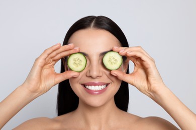 Photo of Woman holding pieces of cucumber on light grey background. Spa treatment