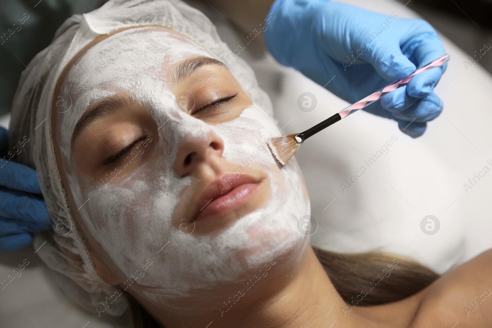 Photo of Cosmetologist applying mask on client's face in spa salon, closeup