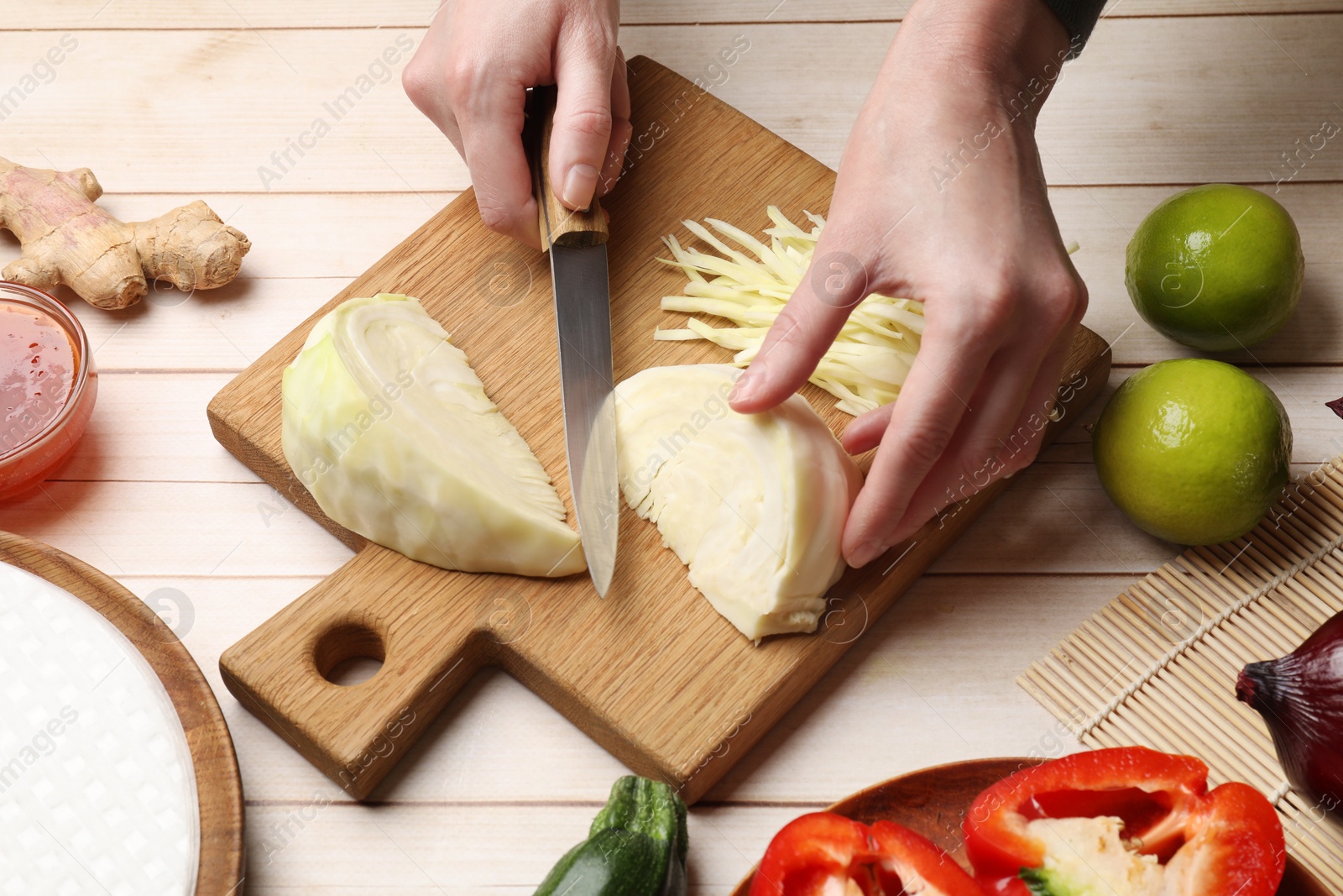 Photo of Making delicious spring rolls. Woman cutting cabbage at wooden table, closeup