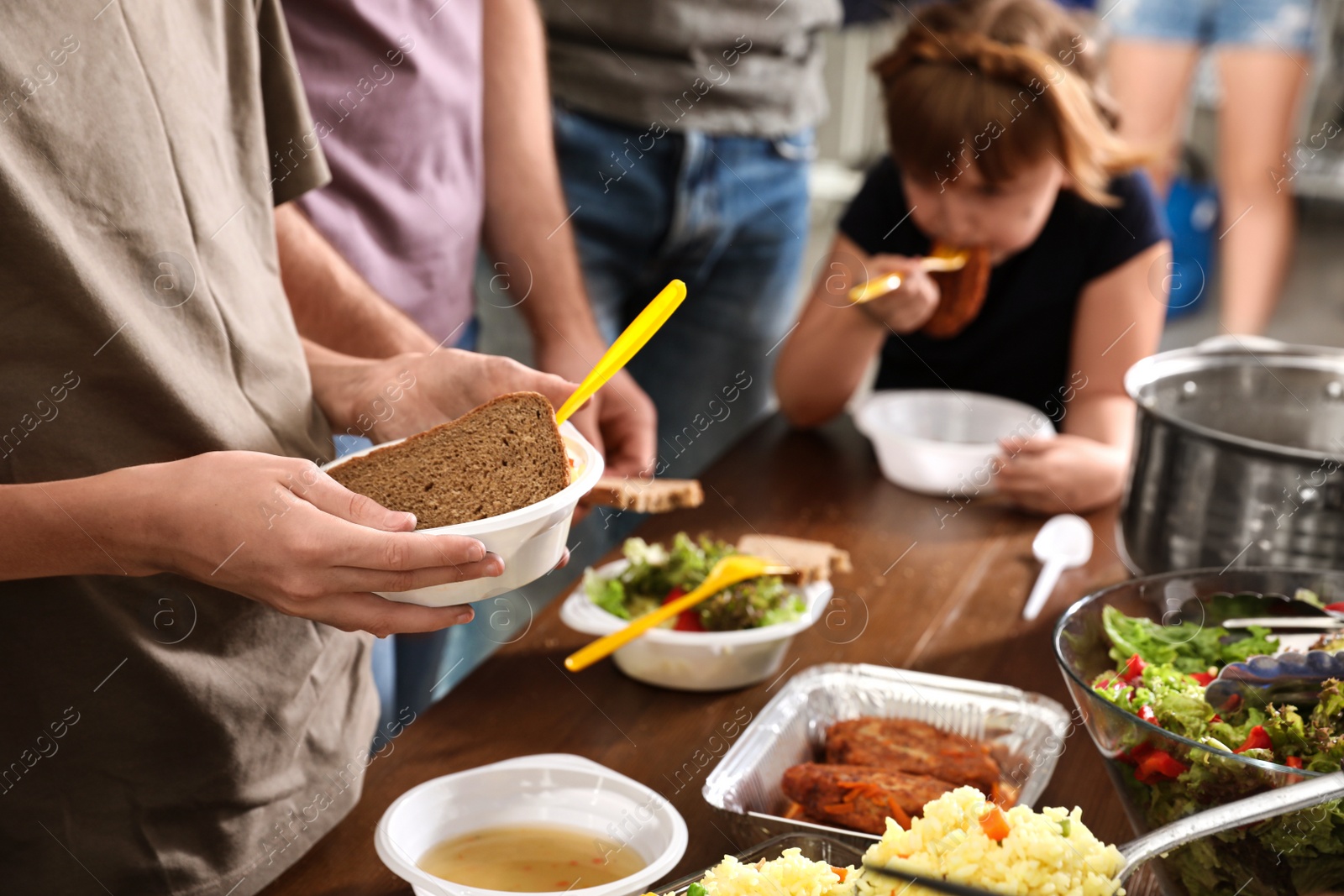 Photo of Little boy holding plate with food for poor people at table in charity centre, closeup