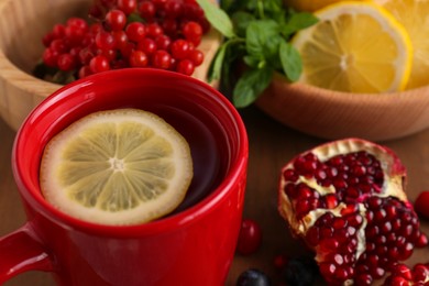 Photo of Cup with delicious immunity boosting tea and ingredients on wooden table, closeup