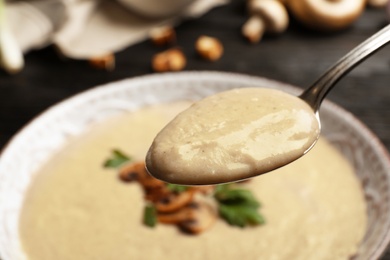 Photo of Spoon with fresh homemade mushroom soup over bowl, closeup