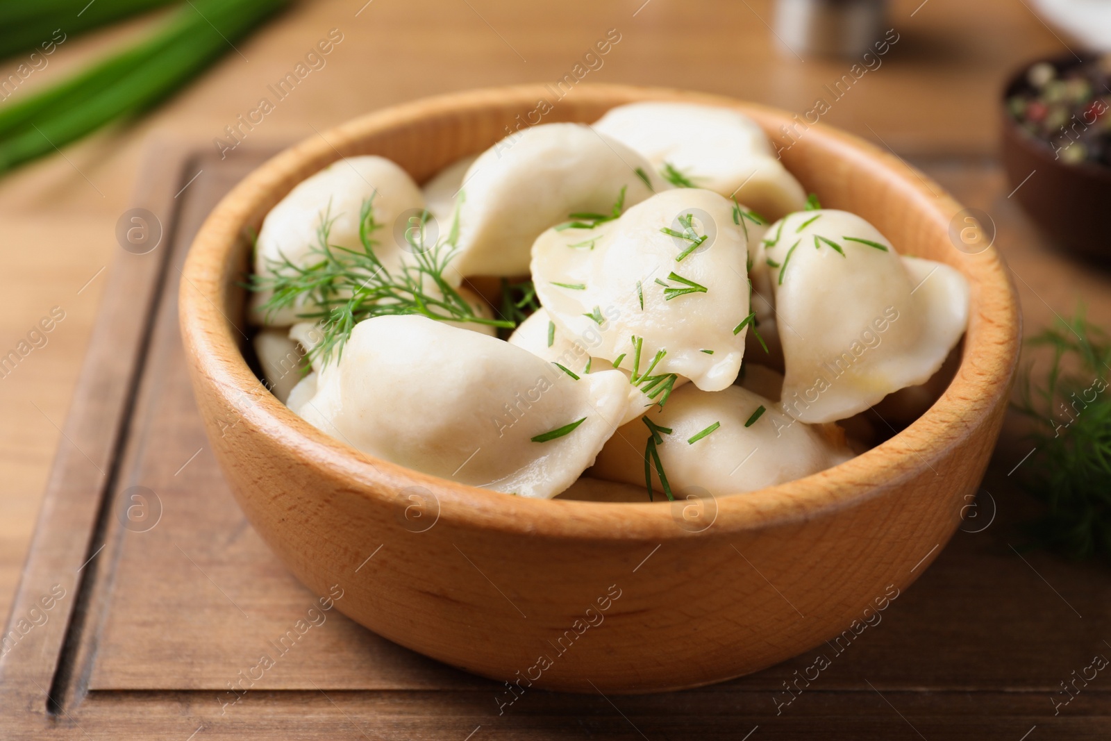 Photo of Bowl of tasty cooked dumplings on wooden board