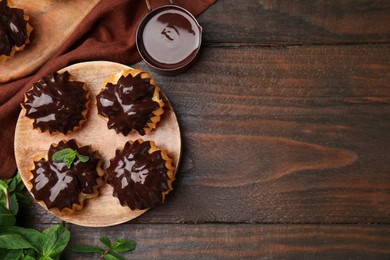 Photo of Delicious profiteroles with chocolate spread and mint on wooden table, flat lay. Space for text