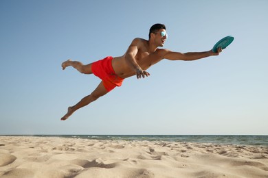 Photo of Sportive man jumping and catching flying disk at beach
