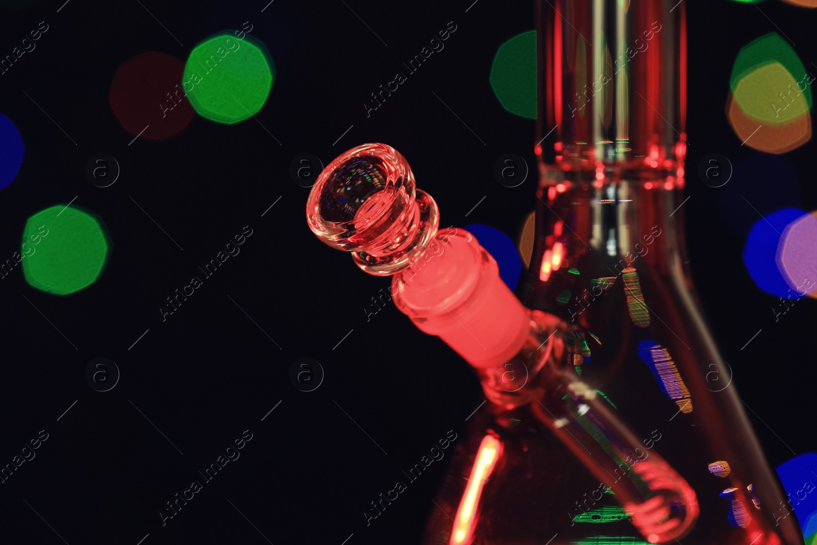 Photo of Closeup view of glass bong against blurred lights. Smoking device