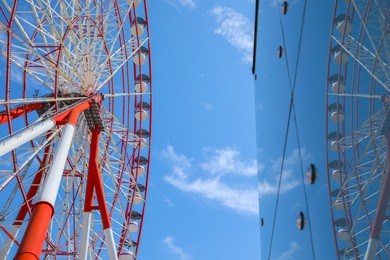 Photo of Beautiful large Ferris wheel near building against blue sky, low angle view