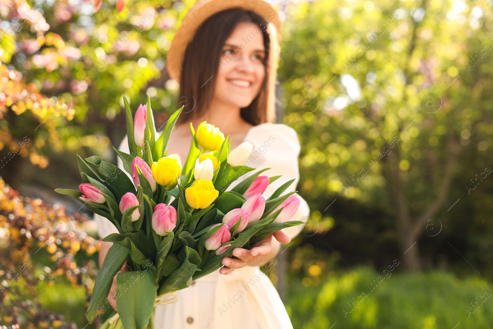 Photo of Beautiful young woman with bouquet of tulips in park, focus on flowers. Space for text