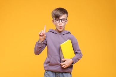 Photo of Surprised schoolboy in glasses holding books on orange background