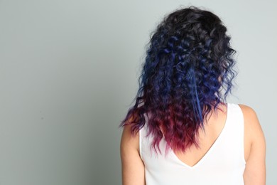 Photo of Young woman with bright dyed hair on grey background, back view. Space for text