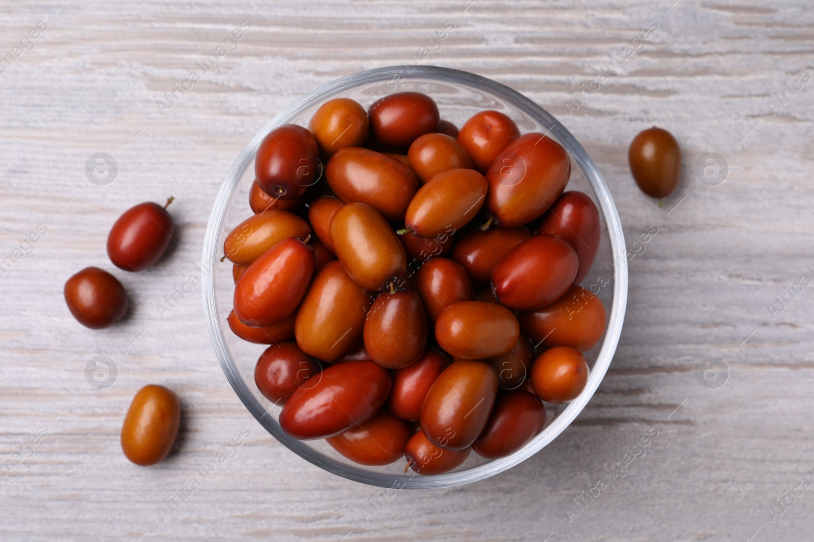 Photo of Fresh Ziziphus jujuba fruits with glass bowl on wooden table, flat lay