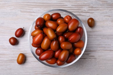 Photo of Fresh Ziziphus jujuba fruits with glass bowl on wooden table, flat lay