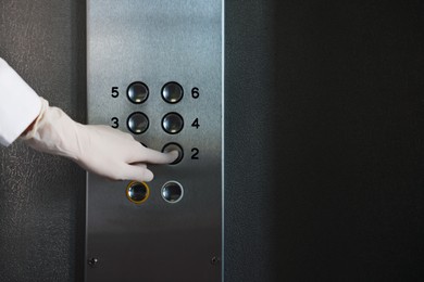 Photo of Woman wearing medical glove choosing floor in elevator, closeup. Protective measure