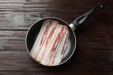 Slices of raw bacon in frying pan on wooden table, top view