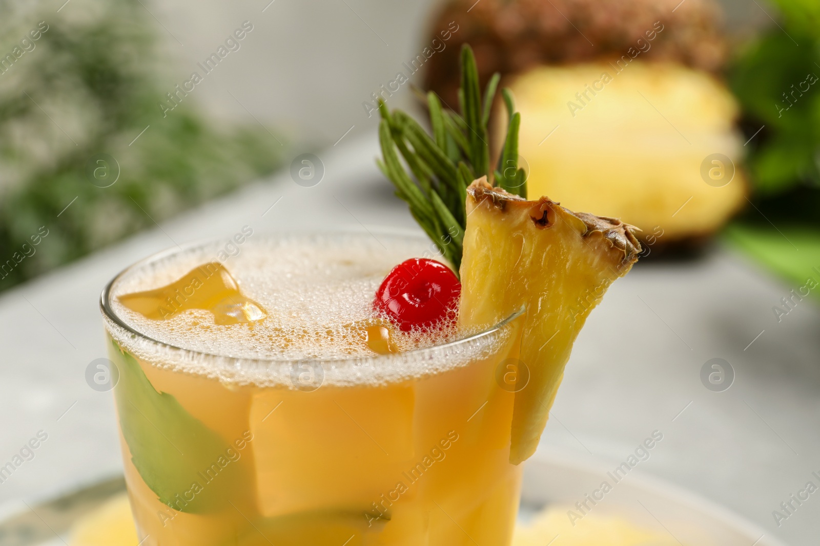 Photo of Glass of tasty pineapple cocktail with rosemary and cherry on light background, closeup