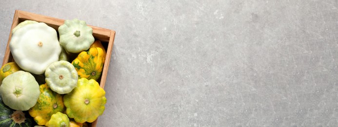 Fresh ripe pattypan squashes in wooden crate on light grey table, top view with space for text. Banner design