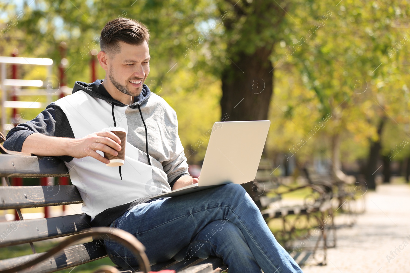 Photo of Portrait of young man with laptop and cup of coffee on bench in park