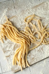 Photo of Raw homemade pasta and flour on light tiled table, top view