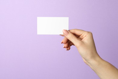 Woman holding blank business card on violet background, closeup. Mockup for design