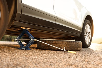 Photo of Car lifted by scissor jack and spare wheel on roadside