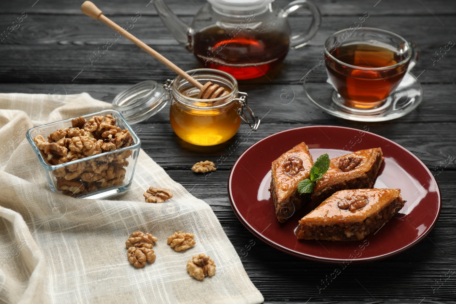 Photo of Delicious sweet baklava with walnuts, mint and hot tea on black wooden table