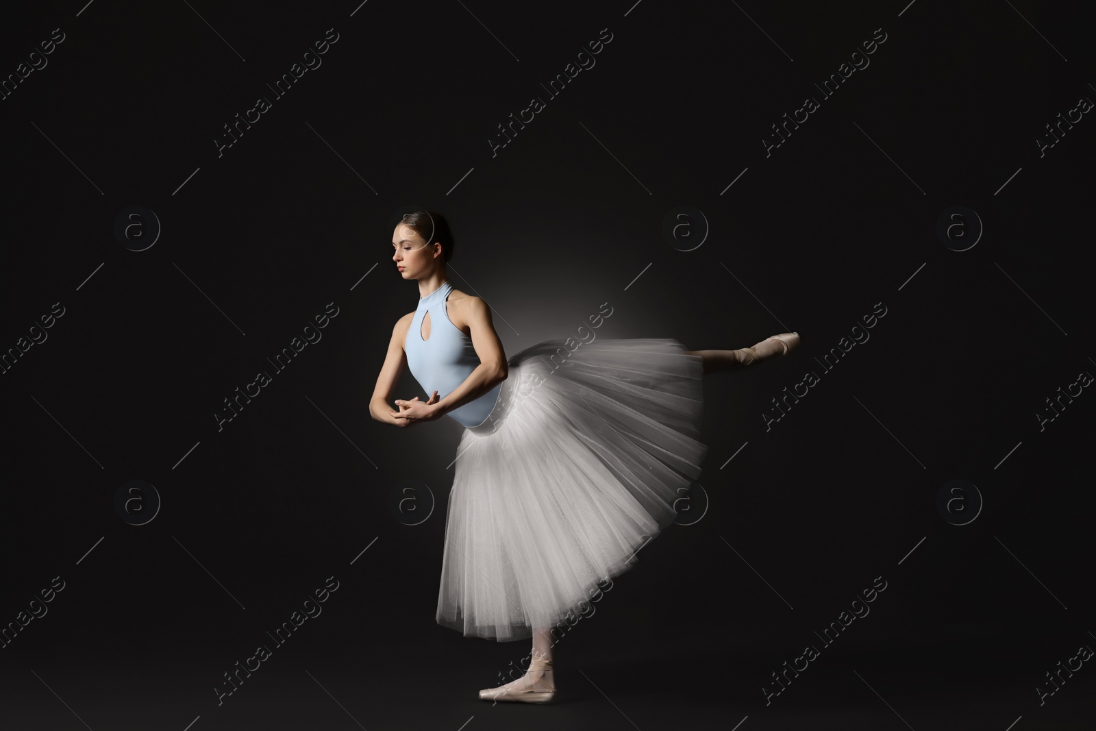 Photo of Young ballerina practicing dance moves on black background