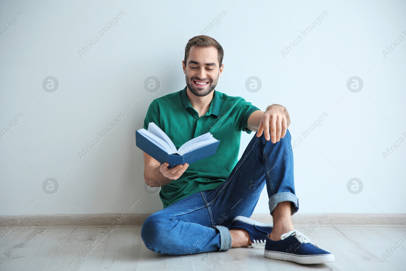 Photo of Young man reading book on floor near wall