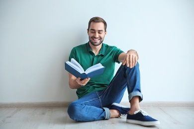 Young man reading book on floor near wall