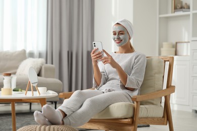 Young woman with face mask using smartphone at home. Spa treatments