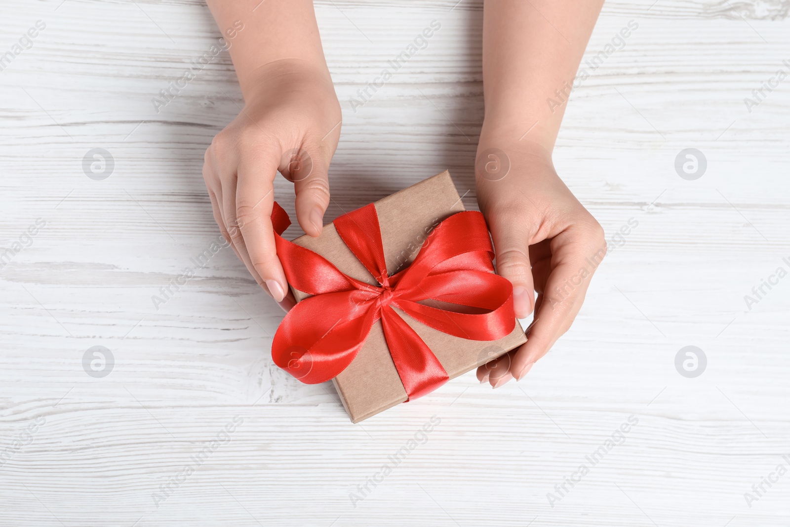 Photo of Woman with gift box at white wooden table, top view