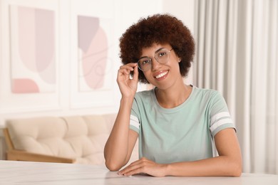 Photo of Happy young woman in eyeglasses at table indoors. Space for text