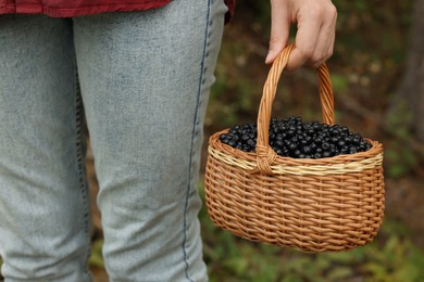 Photo of Woman holding wicker basket with delicious bilberries outdoors, closeup