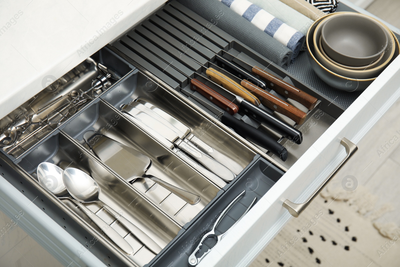 Photo of Open drawer of kitchen cabinet with different utensils, dishware and towels