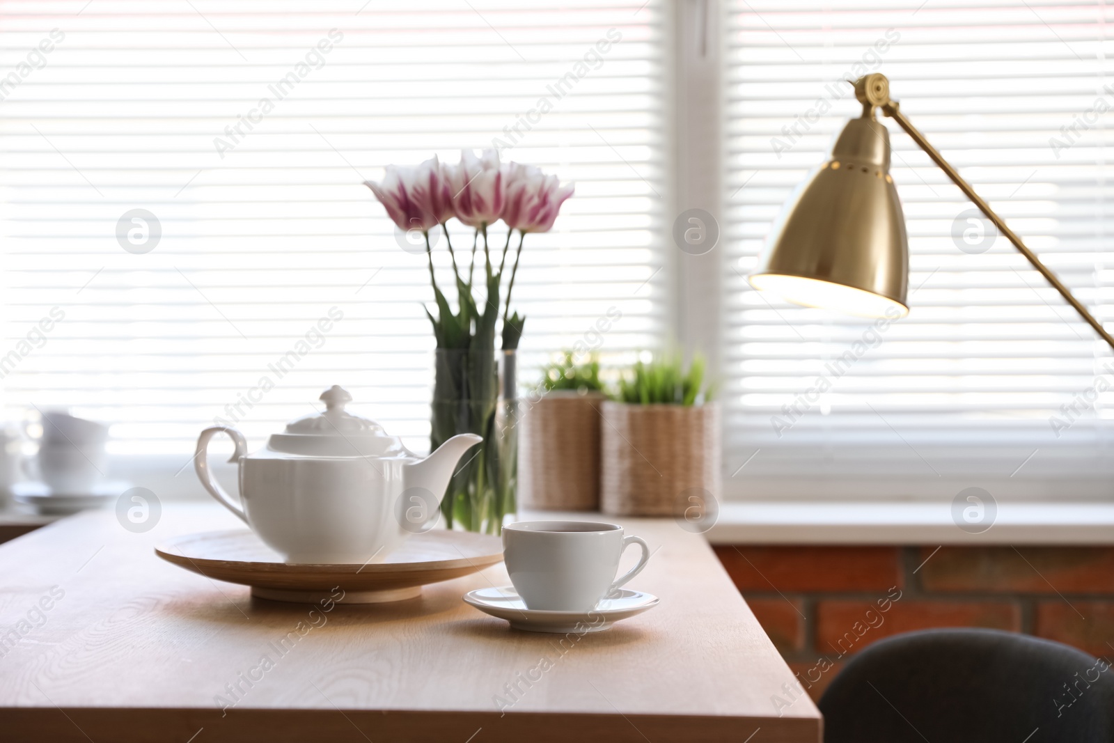 Photo of Tea set on table near window with blinds indoors