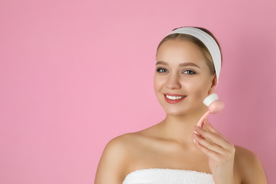 Young woman washing face with cleansing brush on pink background, space for text. Cosmetic product