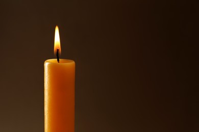 Photo of Burning church wax candle on dark background, closeup. Space for text