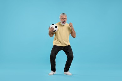 Happy senior sports fan with soccer ball on light blue background