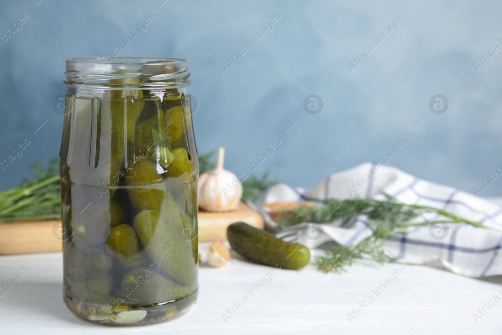 Photo of Jar with pickled cucumbers on white wooden table against blue background, space for text