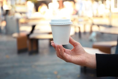 Photo of Woman holding cardboard cup with coffee on city street, closeup. Space for text