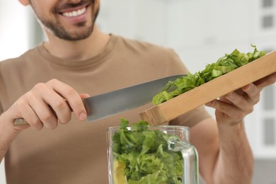 Photo of Man adding cut spinach for delicious smoothie indoors, closeup